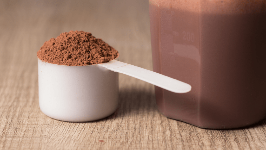 chocolate powder in a cup and a spoon next to it on a wooden table