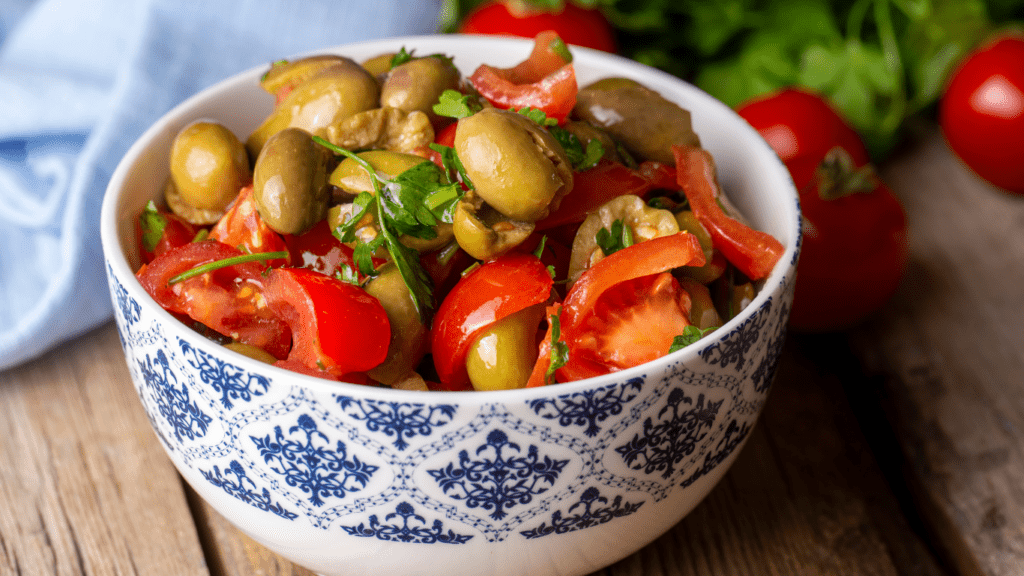 salad with olives and tomatoes in a blue and white bowl on a wooden table